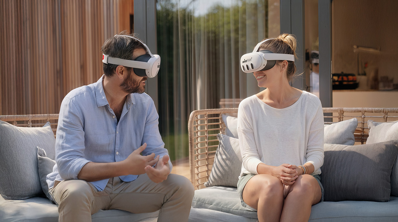 A man and a woman wearing VR headsets, seated on a couch, engaged in conversation.