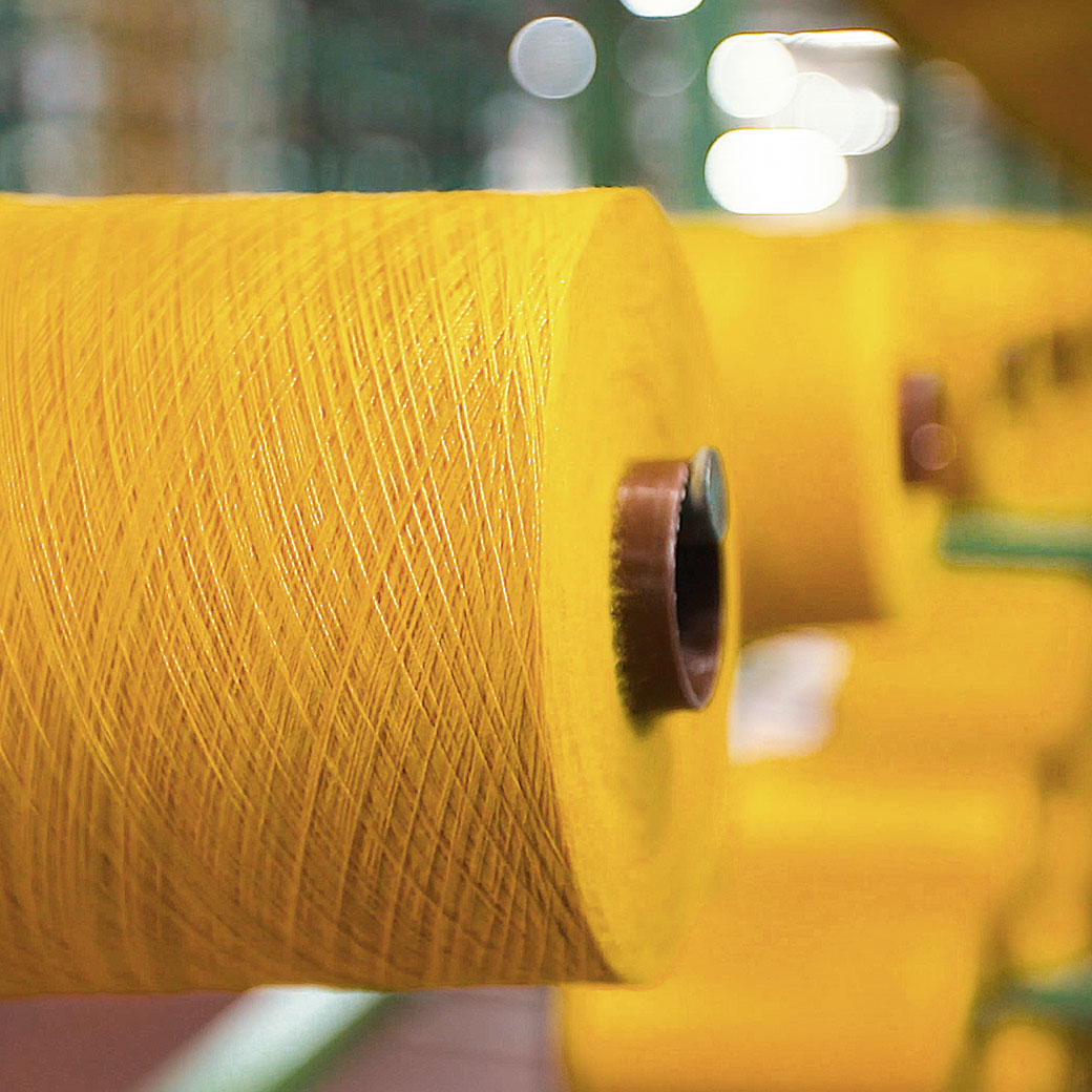 Gelber Spulen-Kegel mit feinen Fäden in einem industriellen Umfeld.