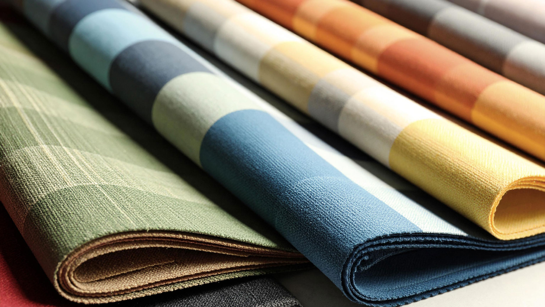A collection of rolled fabrics in various colours and patterns, featuring stripes and blocks.