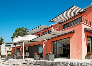 A modern building with multiple awnings, large windows, and a bright blue sky. 