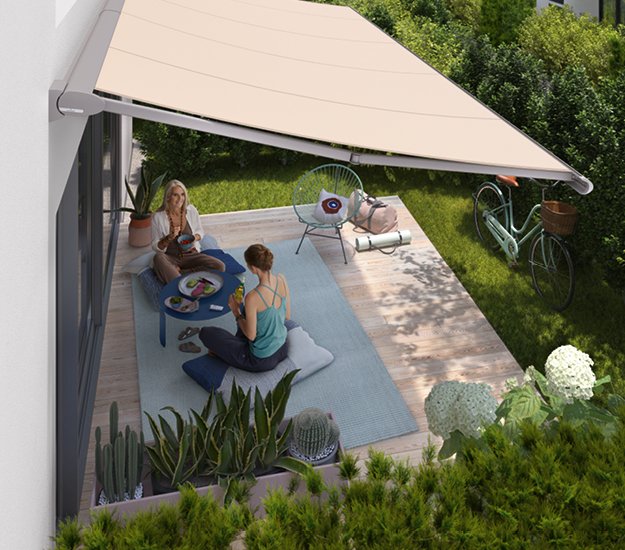 Two women enjoying a meal under a beige awning in a garden setting with plants and greenery. 