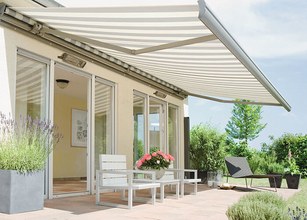 A terrace with a striped awning, featuring seating and vibrant plants in pots. 