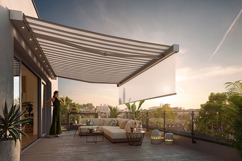 A spacious terrace with a large awning casting shadows, greenery in planters, and a comfortable seating area.