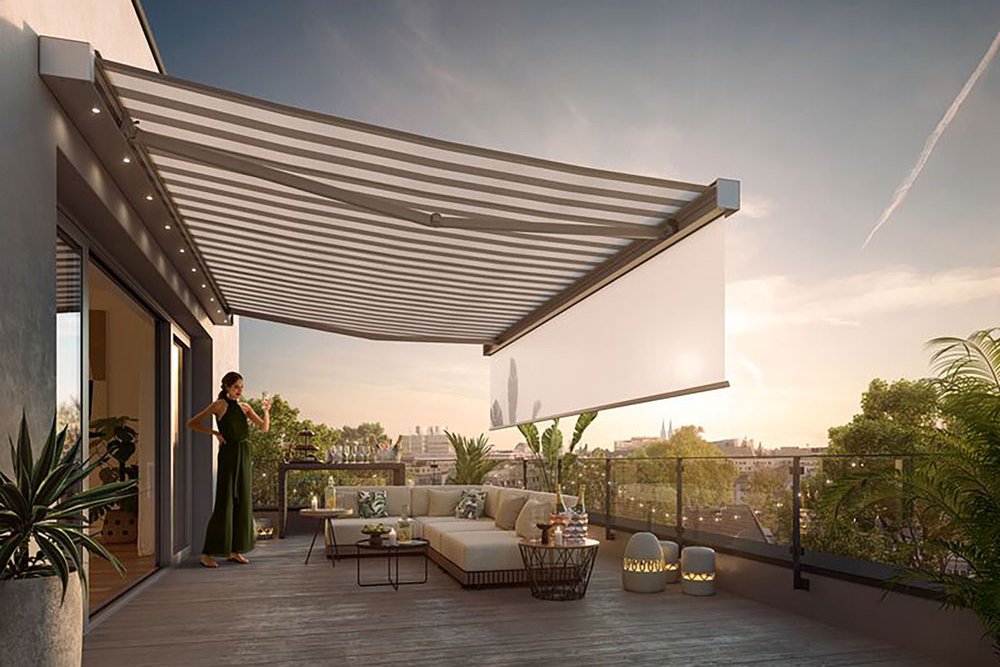 A spacious terrace with a large awning casting shadows, greenery in planters, and a comfortable seating area.