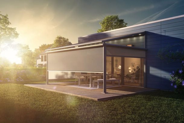A modern home extension with a glass facade and an outdoor area, set against a sunset.