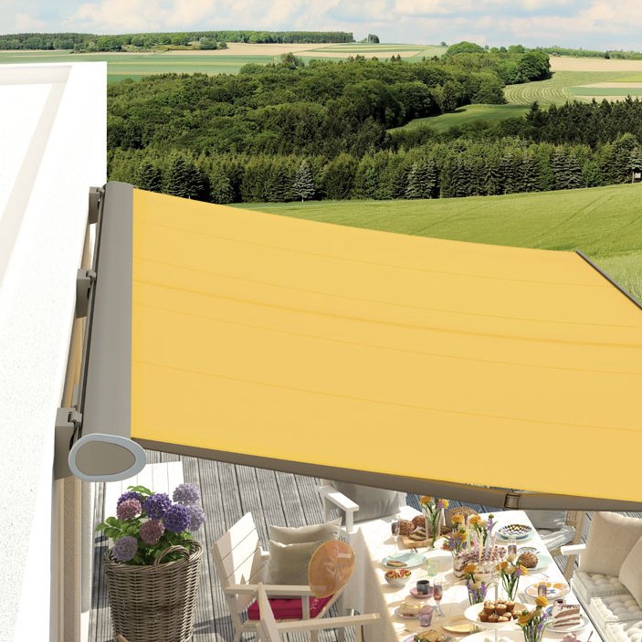 A bright yellow awning extended over a terrace with dining arrangements and a view of green fields.