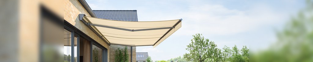 A modern awning extends over a patio, framed by greenery and a clear sky in the background.