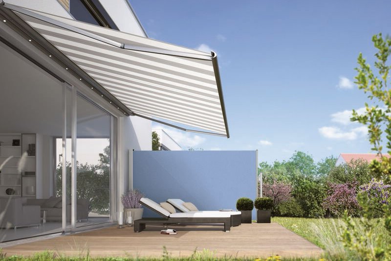 A stylish terrace with a retractable awning and loungers, surrounded by greenery and a blue wall. A stylish terrace with a retractable awning and loungers, surrounded by greenery and a blue wall.