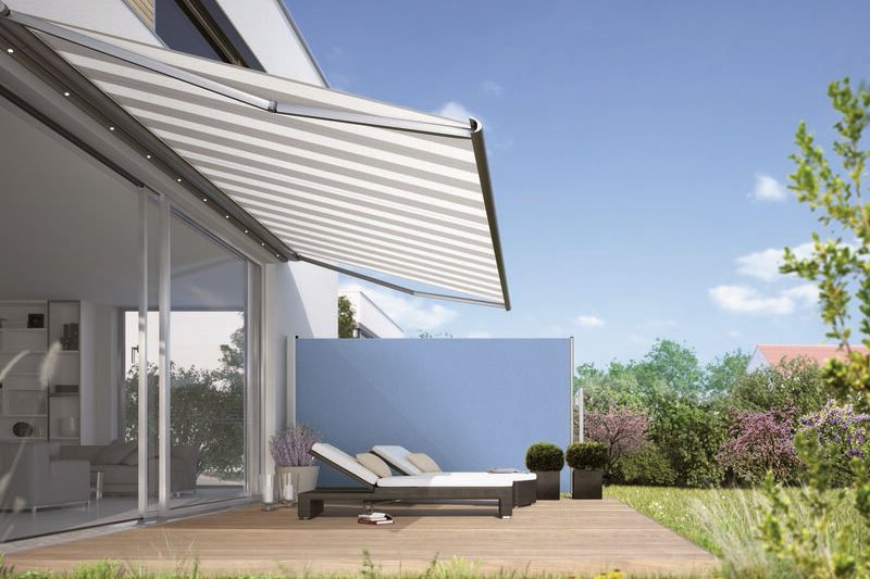 A stylish terrace with a retractable awning and loungers, surrounded by greenery and a blue wall. A stylish terrace with a retractable awning and loungers, surrounded by greenery and a blue wall.