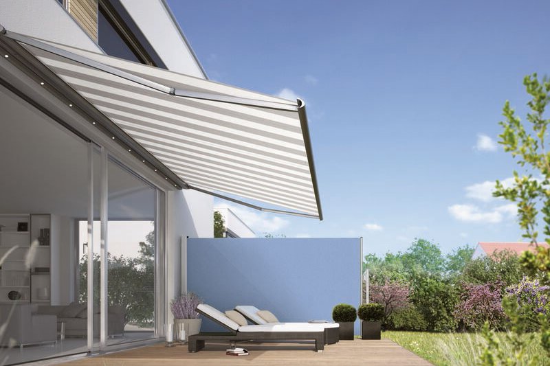 A stylish terrace with a retractable awning and loungers, surrounded by greenery and a blue wall.