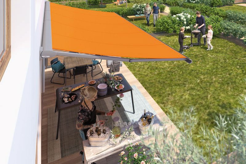 An orange awning extending over a terrace and garden setup with people dining and socialising in the background. An orange awning extending over a terrace and garden setup with people dining and socialising in the background.