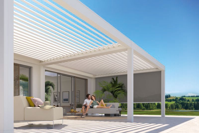 A modern outdoor space featuring a sleek structure with horizontal slats and a patio area. Bright sunlight and greenery.