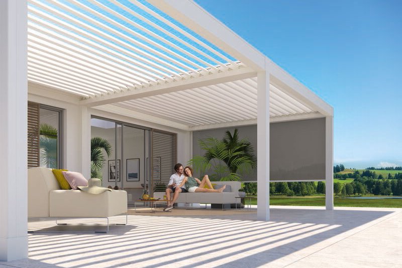 A modern outdoor space featuring a sleek structure with horizontal slats and a patio area. Bright sunlight and greenery.