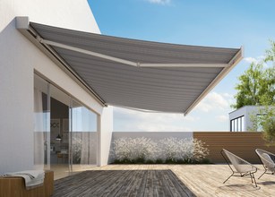Grey awning extending over a wooden terrace with greenery in the background and a modern building structure. 