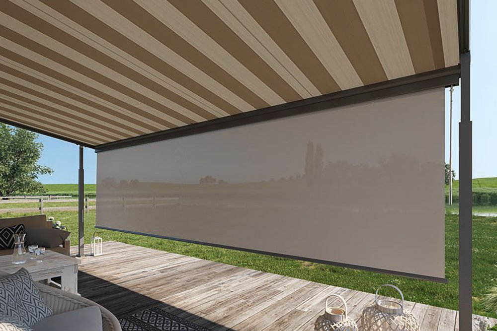 A striped retractable awning above a wooden terrace with a scenic green backdrop.