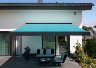 Teal awning extended over a terrace with seating area, attached to a modern house facade. 