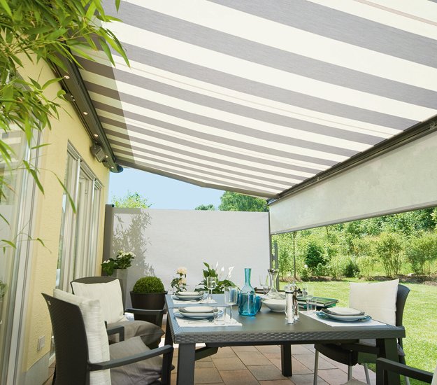 A striped awning provides shade over a dining table set in an outdoor terrace situation. 