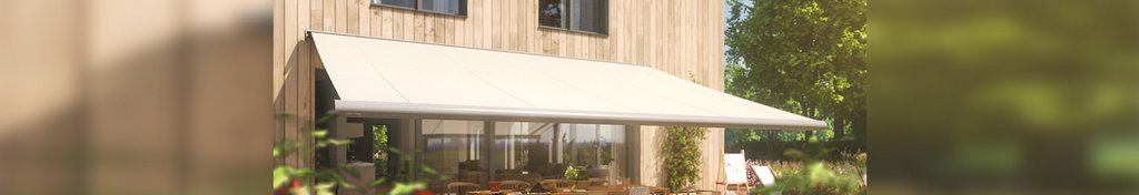A white awning over a terrace area in front of a wooden house surrounded by greenery. A white awning over a terrace area in front of a wooden house surrounded by greenery.