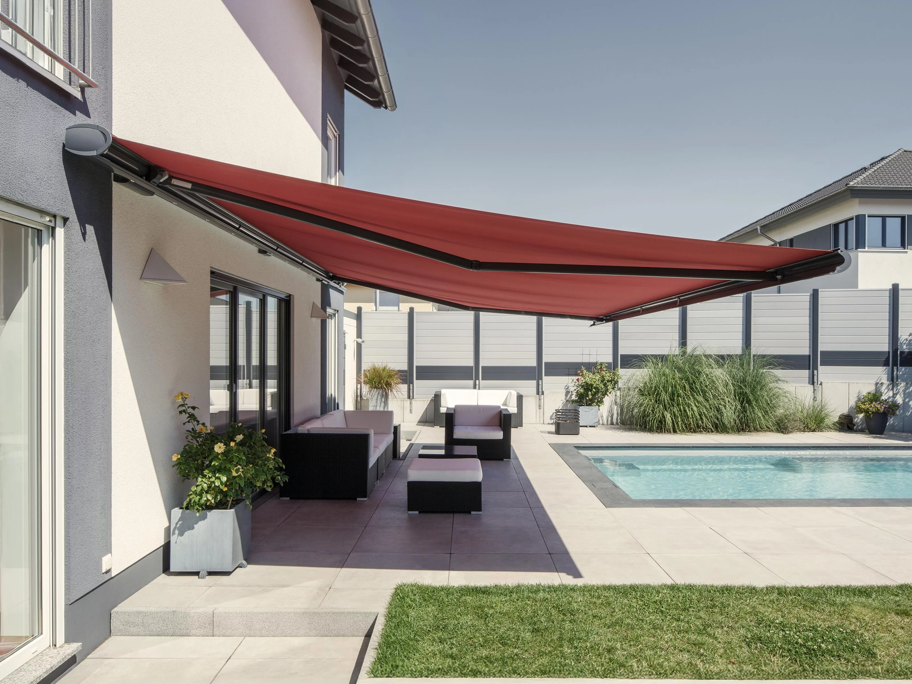 A red awning above a terrace with a swimming pool and landscaped area.