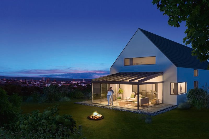 A modern house with a glass extension, surrounded by greenery and a fire pit in the garden at dusk. A modern house with a glass extension, surrounded by greenery and a fire pit in the garden at dusk.