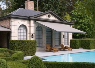 A modern building with a grey awning, surrounded by green hedges and a pool. 