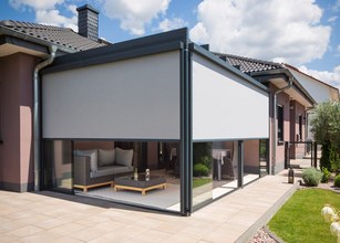 A modern outdoor space featuring a grey shading structure, patio, and glass elements under a blue sky. 