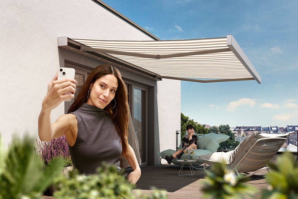 A woman taking a selfie on a balcony with a retractable awning and green plants nearby.