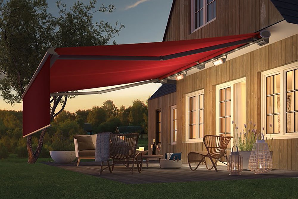 A patio with a red canopy, wooden house, and chairs, surrounded by grass and trees in a peaceful setting.