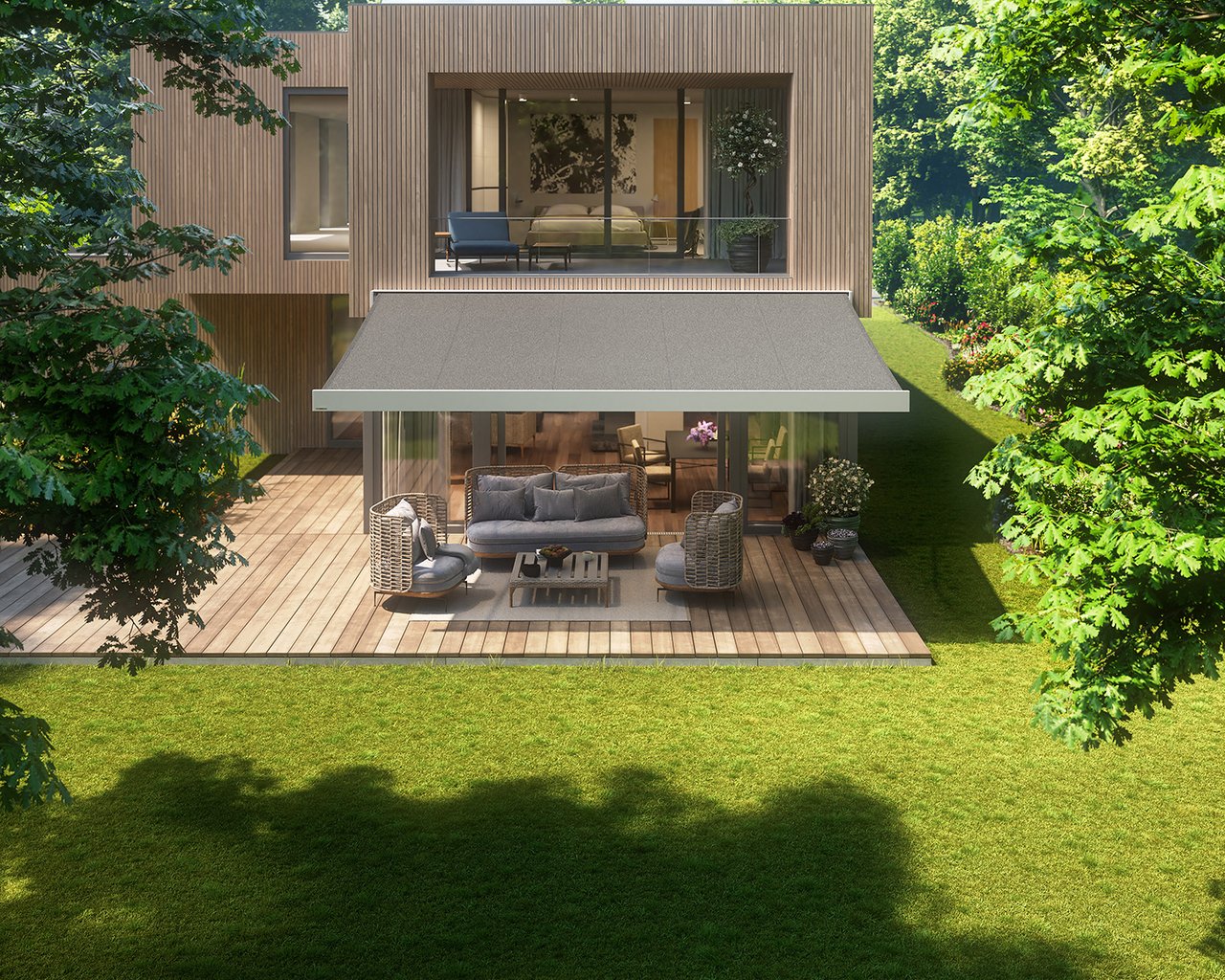 A modern house with a terrace covered by a grey awning, surrounded by greenery.