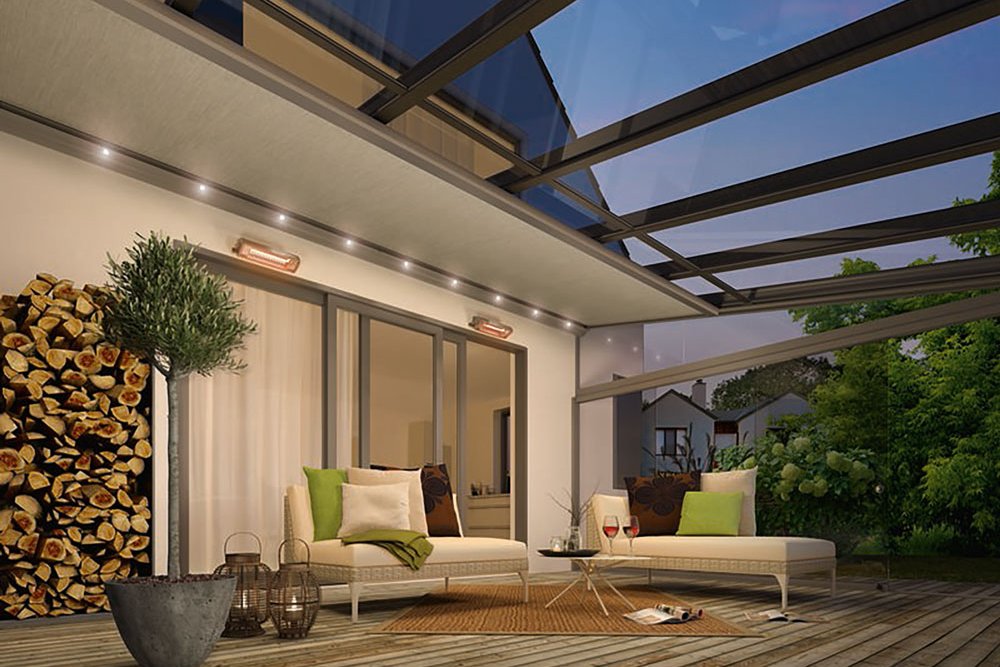 A modern terrace with a glass roof, seating area, and a log stack in a natural setting.