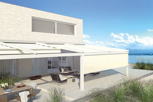 A modern terrace with a white overhead structure and a view of the water, featuring seating and a dining area.