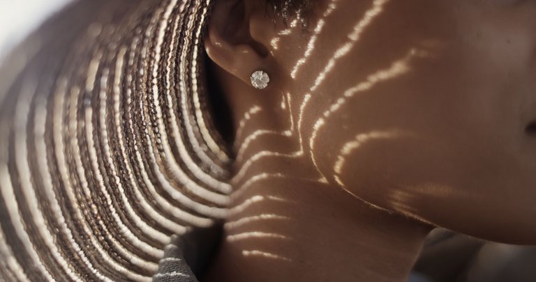 A close-up of a person's ear with a sparkling earring, shadows casting a striped pattern from a hat.