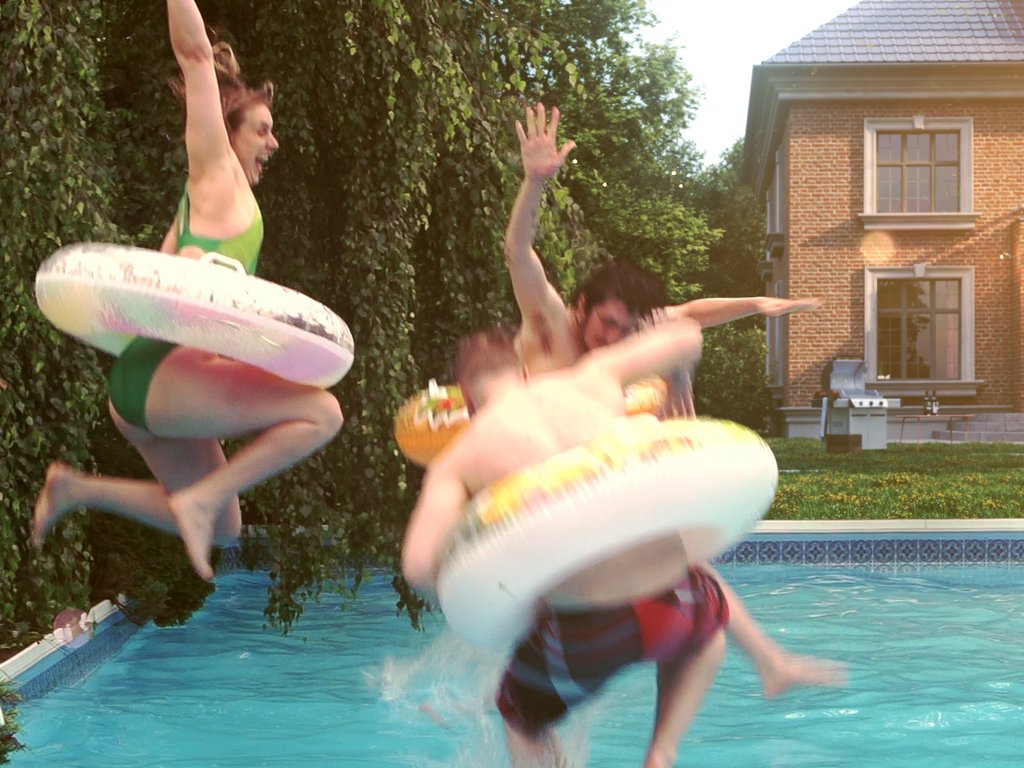 Three people jump into a pool, splashing water with colourful rings.