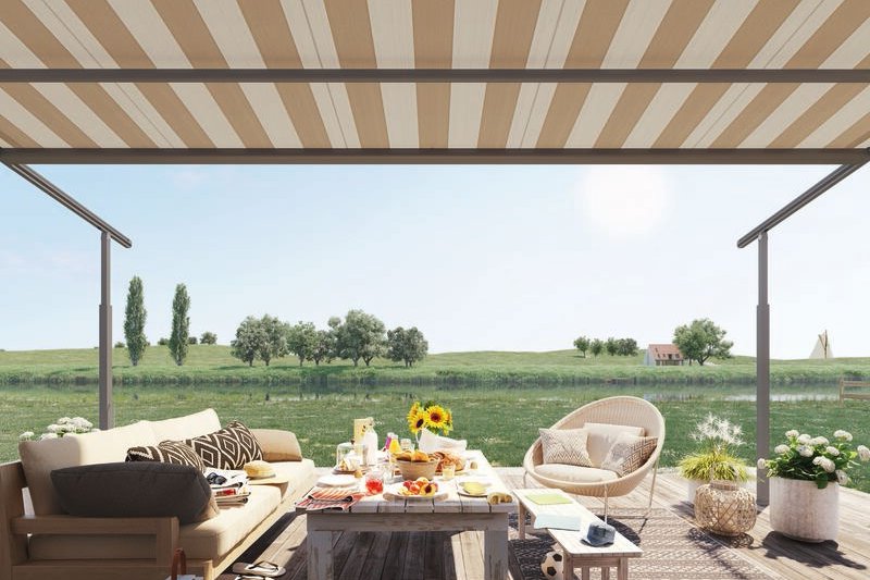 A stylish terrace situation with a striped awning, seating, and a table set for a meal against a green landscape.