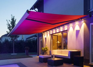 A vibrant red awning extends over a modern outdoor seating area, illuminated by soft lights. 