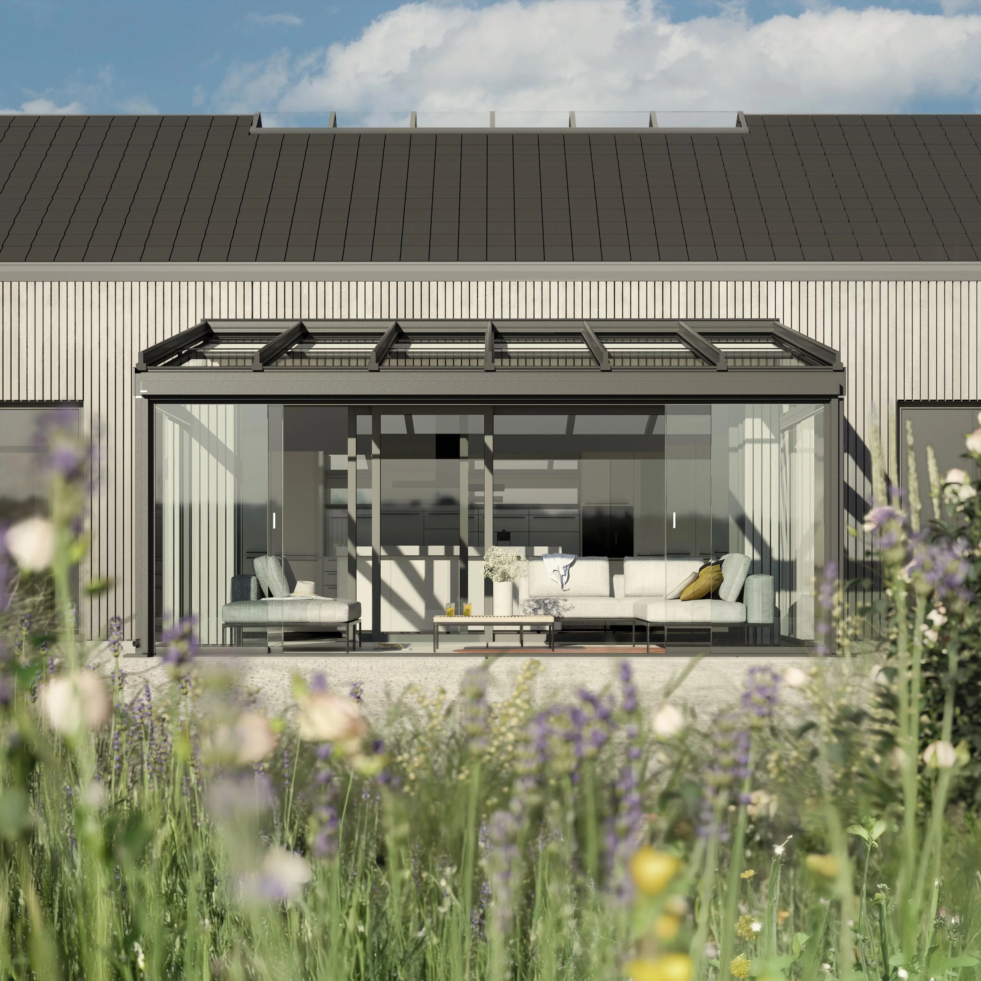 A modern facade with a glass extension and seating area, surrounded by lush greenery.