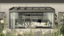 A modern facade with a glass extension and seating area, surrounded by lush greenery.