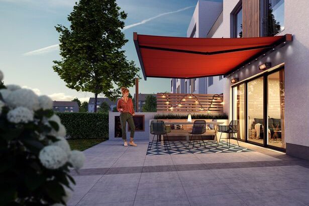 A modern patio with a red awning, greenery, and contemporary architecture in a twilight setting.