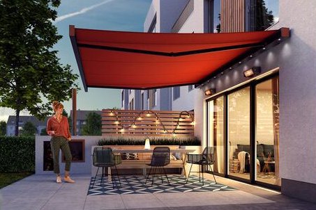 A modern patio with a red awning, greenery, and contemporary architecture in a twilight setting.