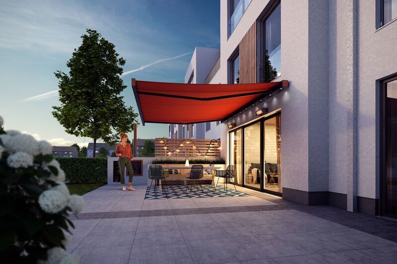 A modern patio with a red awning, greenery, and contemporary architecture in a twilight setting.