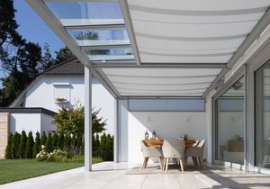 A modern terrace with an awning, dining area, and sliding glass doors in a sunny garden setting.