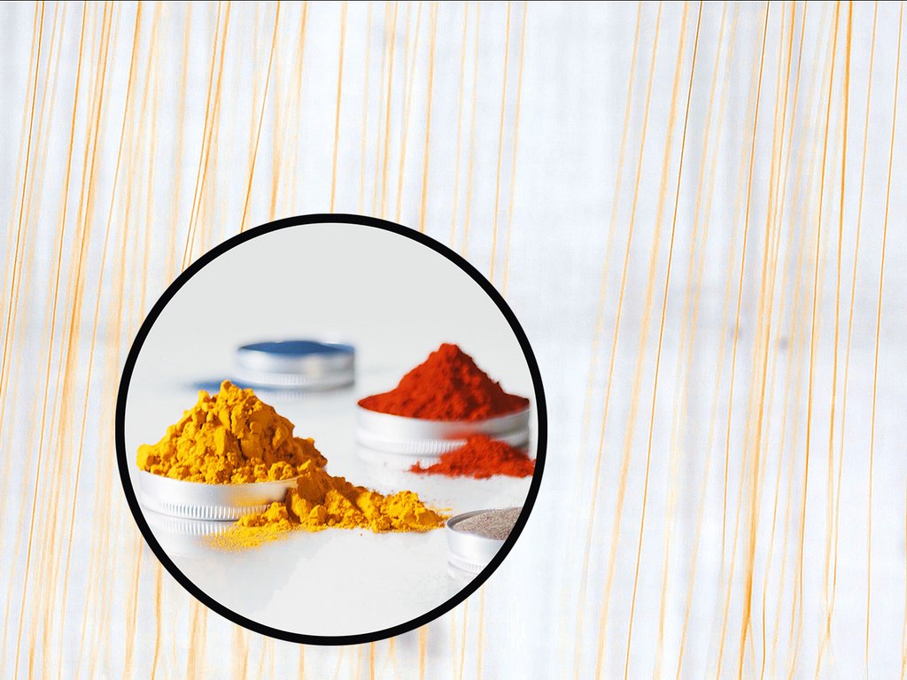 Piles of yellow and red powders inside circular containers on a light background.