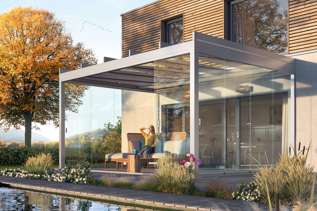 Modern glass extension with a flat roof, surrounded by greenery and a pond. Warm tones from an autumn tree.