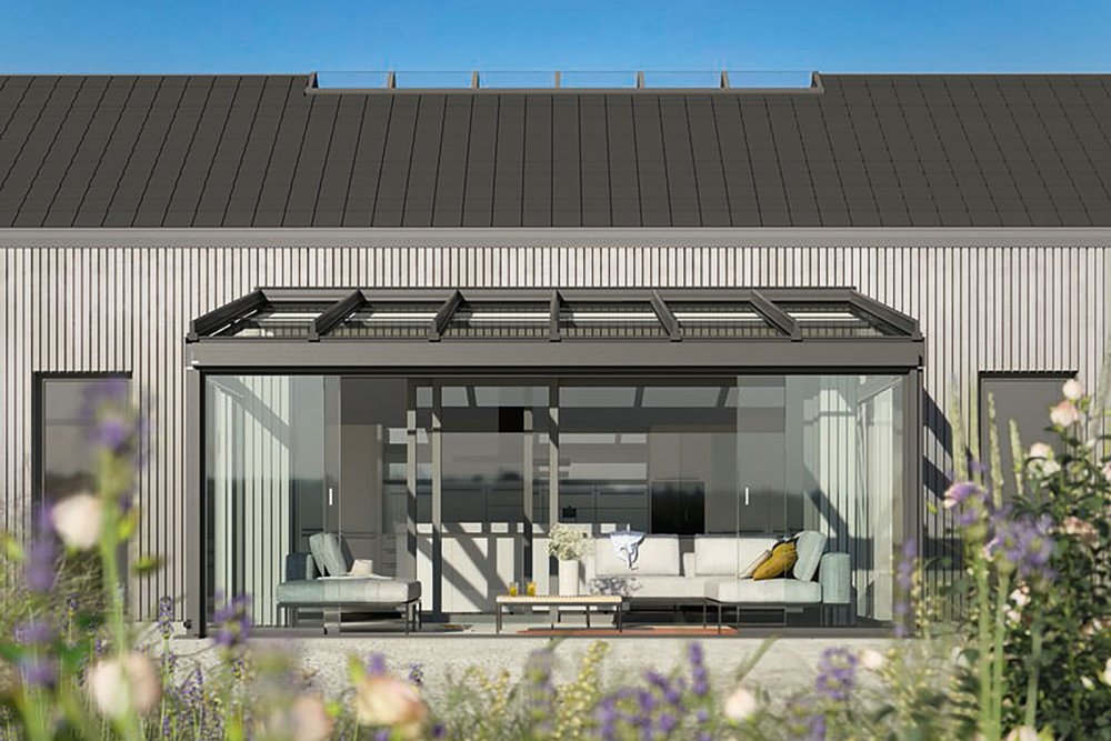 Modern house façade with a glass extension and a black roof, set against a clear blue sky.