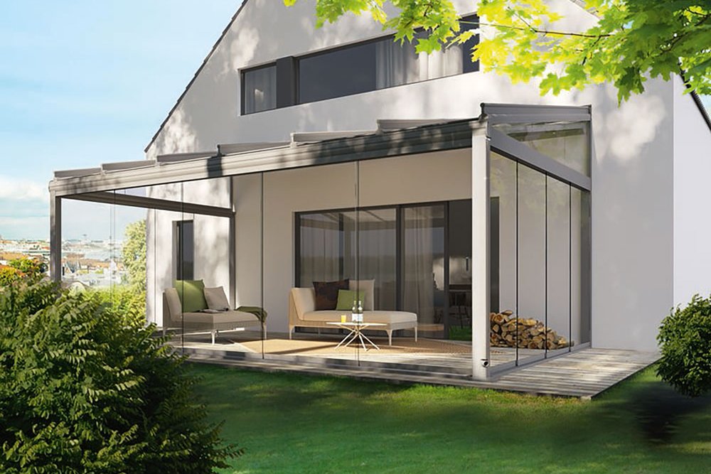 A modern house with a terrace featuring a sleek overhang, large windows, and greenery surrounding it.