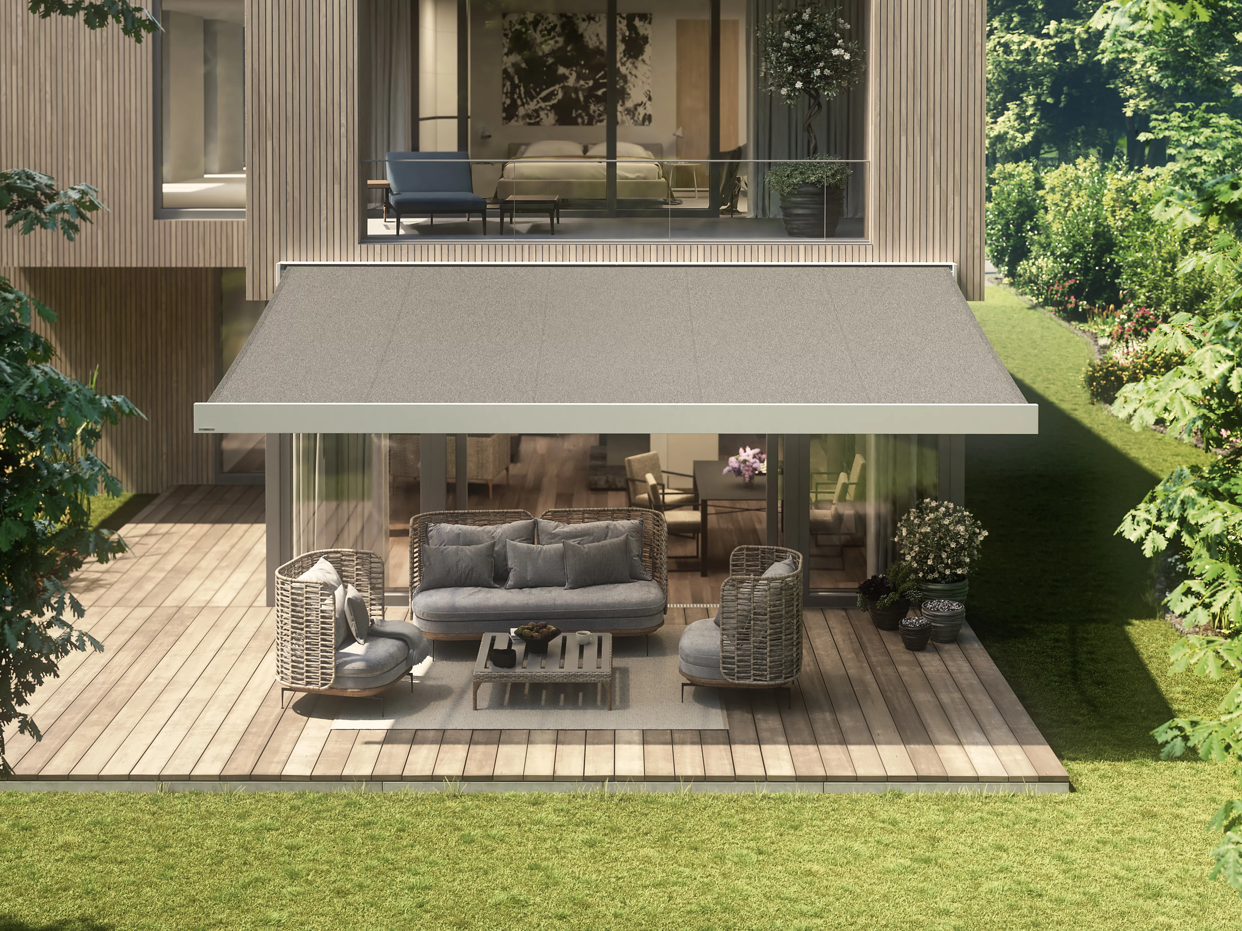 A modern home with a grey awning over an outdoor seating area, surrounded by greenery.