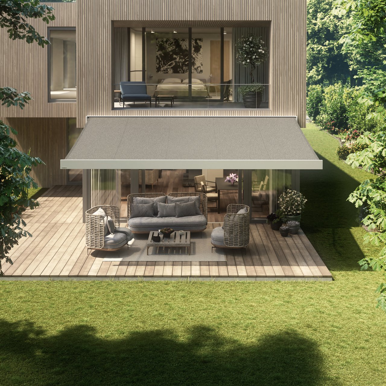 A modern home with a grey awning over an outdoor seating area, surrounded by greenery.