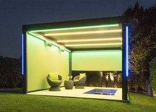 A modern outdoor structure with green illumination and seating, featuring a pool in a garden setting. 