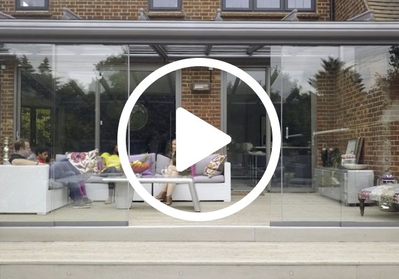 Indoor seating area with glass elements, a play button overlay, and people relaxing.