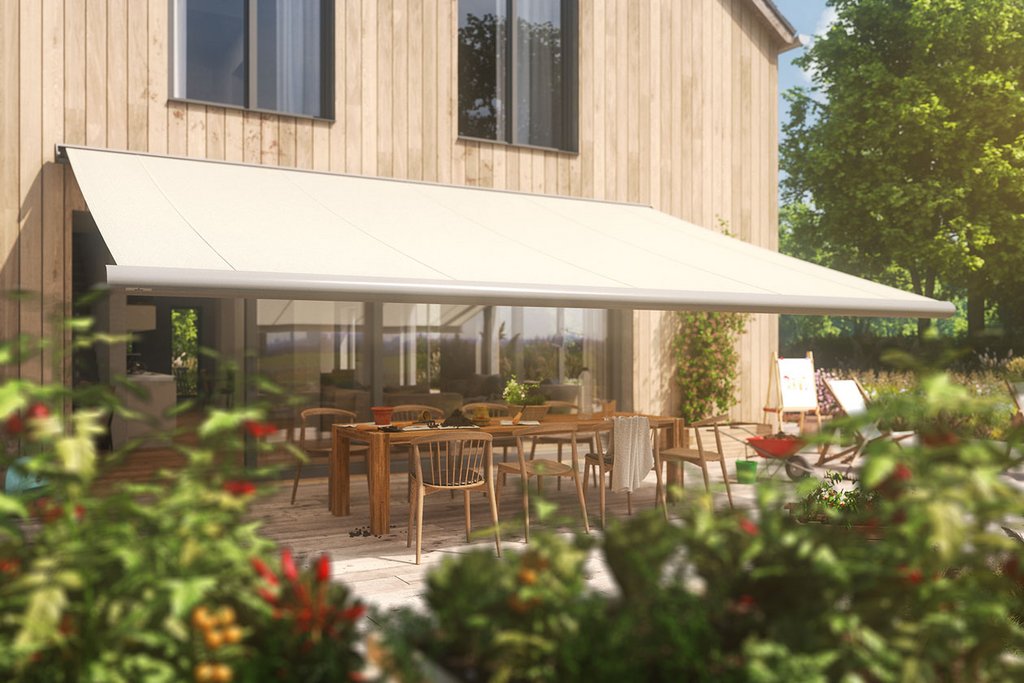 A beige awning covers a terrace with wooden furniture and vibrant plants in a sunny outdoor setting.
